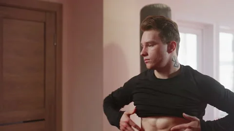 Man in gym environment wearing a black long sleeve shirt over head Vídeo Stock 325965065