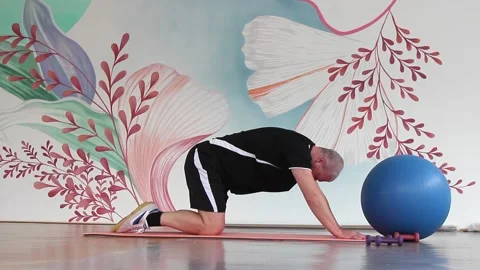 A man in a gym on a mat doing exercises to stretch the back muscles in a deflect Vidéo 150796825