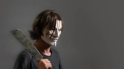 A man in a hacker or anonymous mask holds a machete on his shoulder. The guy  Stock Photos