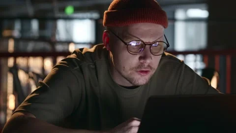 A man hacker sitting at a laptop in a dark room and swearing at the screen Stock Footage 260718976