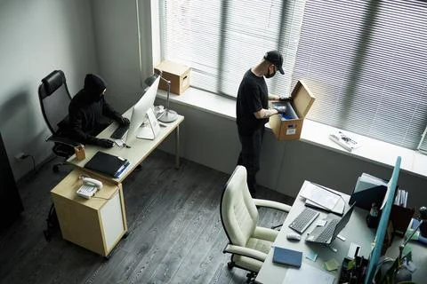 Man Hacking into Office Computer and Accomplice Rummaging through Documents Stock Photos