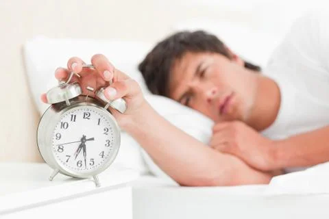 Man half awake as he silences his alarm clock as its about to fall over Stock Photos
