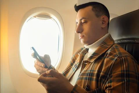 A man in a half-empty plane with a phone. Guy traveler looking at smartphone. Stock Photos
