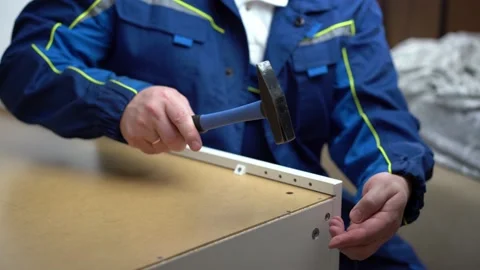 A man hammers a nail into the back wall, assembles a white cabinet Stock Footage 202302970