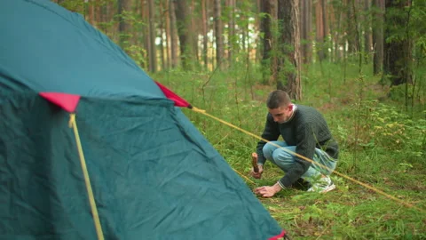 Man Hammers Tent Peg into Ground During Forest Camping Setup Vídeo Stock 310483272