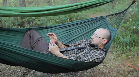 A man in a hammock making selfie on the phone. Man in the woods with a beard and Stock Footage 64482547
