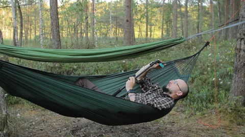 A man in a hammock making video on selfie stick with action camera. Man in the Stock Footage 64481375