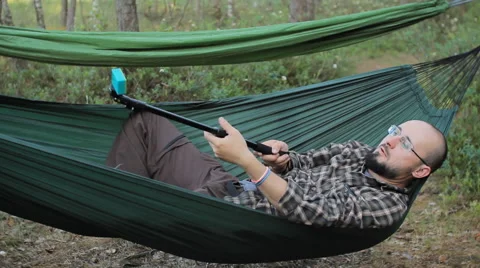 A man in a hammock making video on selfie stick with action camera. Man in the Stock Footage 64483846