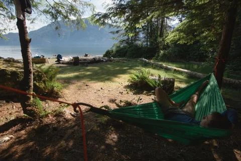 Man in hammock under trees on beach near lake Stock Photos