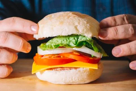 Man hand assembling a hamburger made of meat, cheese, tomato, onion rings, le Stock Photos