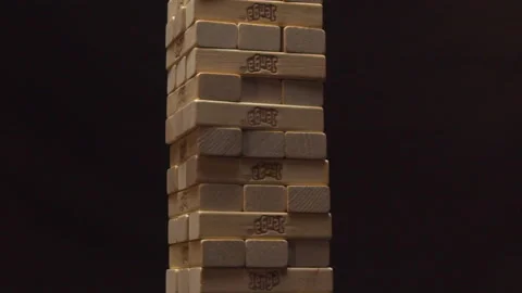 Man hand breaks Jenga tower on grey table in dark room Stock Footage 162187548