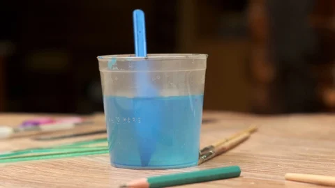 Man hand cleans brush in plastic cup with water on table Stock-Footage 127837482