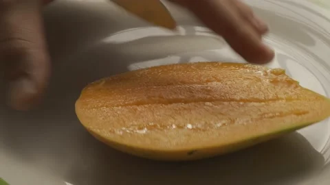 A man hand cuts ripe mango into cubes on a white plate with a sharp knife Видео 232970003