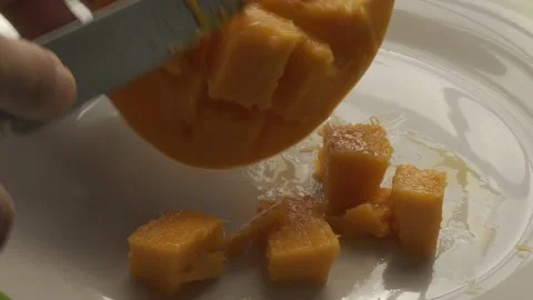 A man hand cuts ripe mango into cubes on a white plate with a sharp knife Stock Footage 233007652
