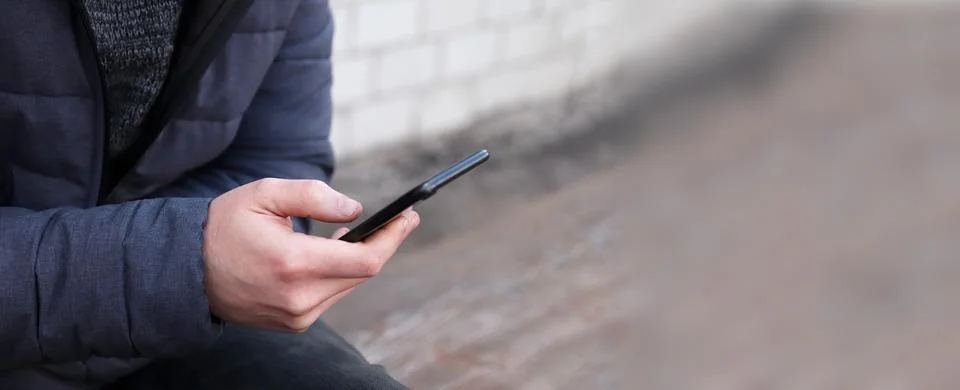 Man hand holding and using black smartphone closeup on outdoor background. .. Stock Photos
