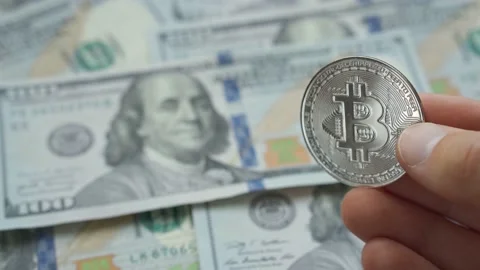 Man hand holding crypto currency silver Bitcoin coin above dollars background Stock Footage 201468328