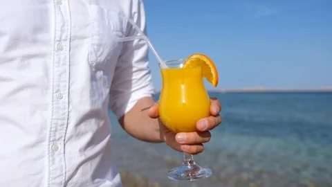 Man Hand Holding Fresh Orange Juice On The Beach By The Sea Video stock 107870706