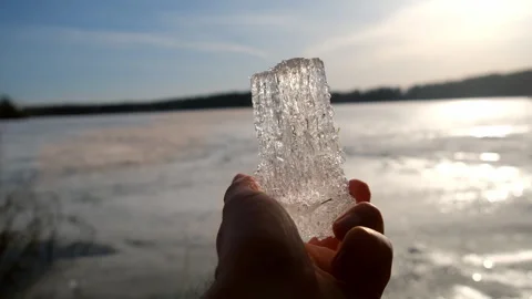 Man hand holding ice block on frozen river background at sunset in camping. Stock Footage 311865456