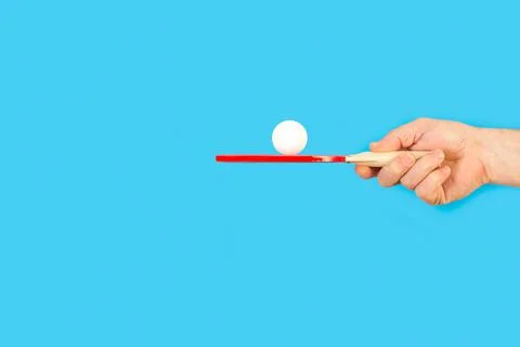 Man hand holding a red ping pong paddle with a white ball on a blue background Foto stock
