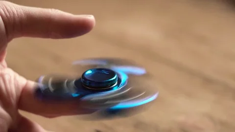 A man hand holds rotating hand spinner or fidget spinner over wooden background Stock Footage