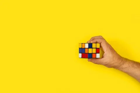 Man hand holing a Rubic cube on a yellow background with copy space Stockfoto's