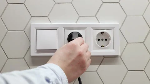 Man hand inserts a plug into black electrical outlet on white wall. Earth Hour Stock Footage 151111349