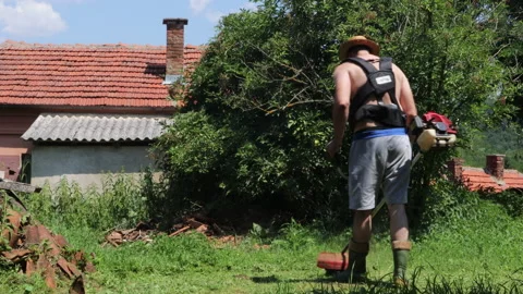 Man with hand lawn mower trimming tall grass in backyard on summer hot day Stock Footage 200847225
