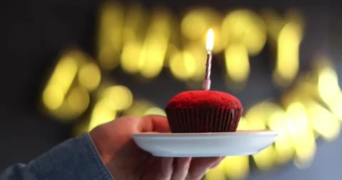 Man hand lights pink candle on red birthday cupcake on black background with  Stock Footage 303345075