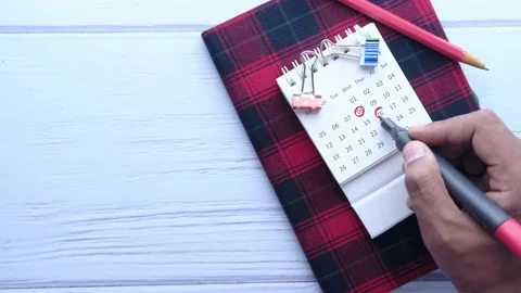 Man hand marking important dates on small calendar with a red pen on wooden.. Stock Footage 333031662