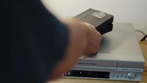 Man hand picking up and inserting cassette into vintage VCR Stock Footage 347141505