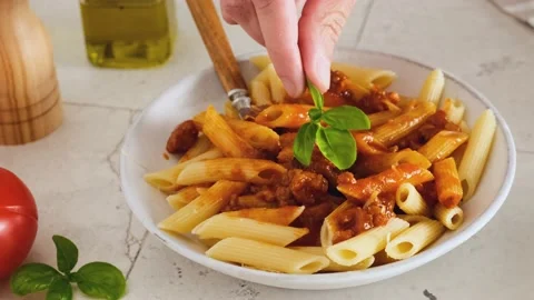 A man hand puts basil in pasta penne with bolognese sauce Stock Footage 196598457