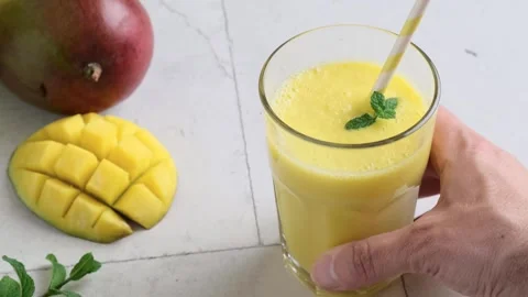 Man hand puts glass of yellow mango smoothie or milkshake with mint and straw on Stock Footage 271238053