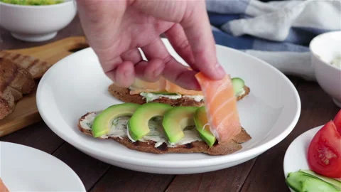 Man hand puts salmon slice on avocado  healthy sandwich close up Stock Footage 125063519