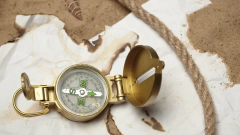 Man hand putting gold compass on burnt maps on sand background close-up, golden Stock Footage 158930890