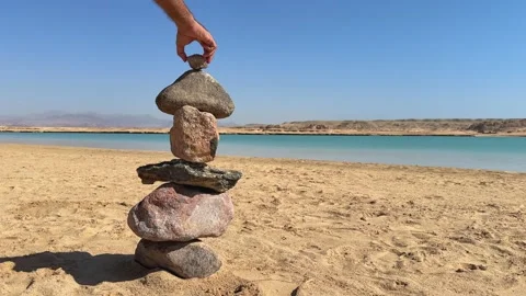 Man hand Stacking Stones in Cairn Pyramid on the Shore of Magic Lake in Ras Stock Footage 341995457