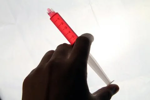 Man Hand with syringe full with red solution medicine over bright light. Medi Stock Photos