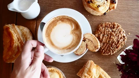 Man Hand Take Cup of Coffee on Breakfast with Croissants on Wooden Table in Cafe Video stock 136829023