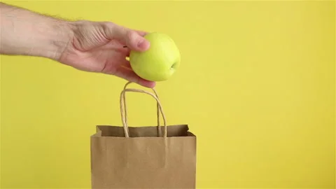 Man hand take a green apple from paper eco bag on yellow background Stock Footage 150313922
