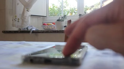 Man Hand Tapping Mobile Phone Screen Resting on Kitchen Table Видео 344207965