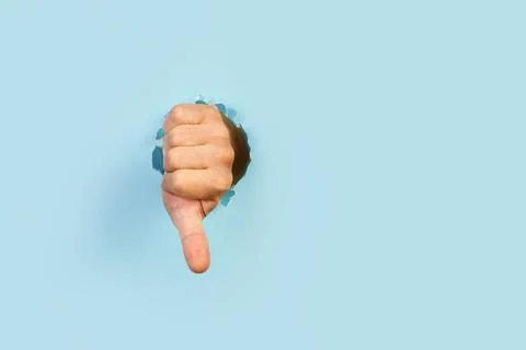 Man hand with thumb down gesture through a hole in a light blue background Foto stock