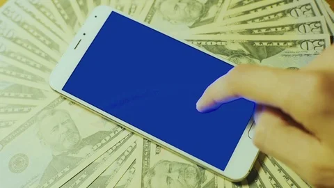 Man hand use blue chroma key touch screen of smartphone on pile of dollar bills Stock Footage 72323058