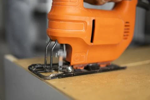 Man hand using electric jigsaw for cutting a fiberboard on a back side of a Stock Photos