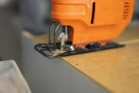 Man hand using electric jigsaw for cutting a fiberboard on a back side of a Stock Photos