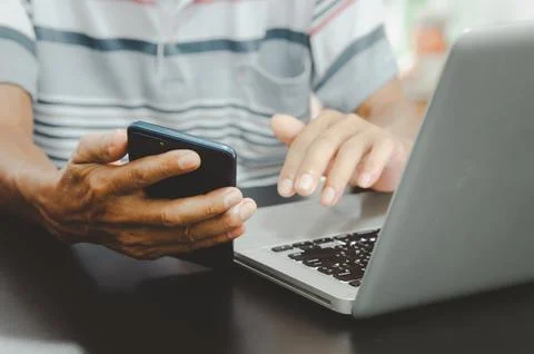 Man hand using smart phoneand laptop on table at home, searching informatio.. Stock Photos