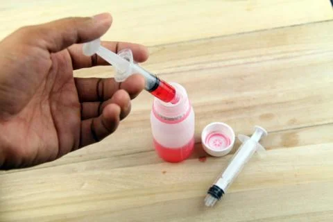 Man hand using syringe to draw sucking red medicine from bottle. Preaparing f Stock Photos