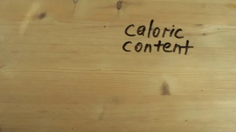 Man hand writes down caloric content of orange on wooden surface Stock Footage 82904945