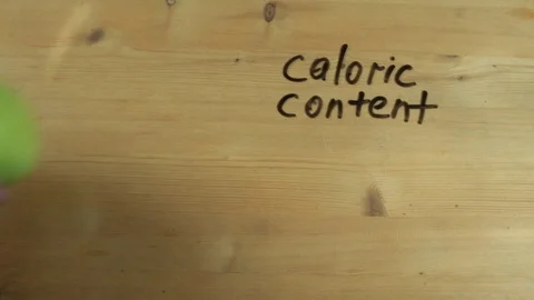 Man hand writes down caloric content of apple on wooden surface Stock Footage 82905556