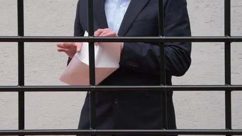 Man handcuffed behind bars holding a piece of paper.  Stock Footage 289305693