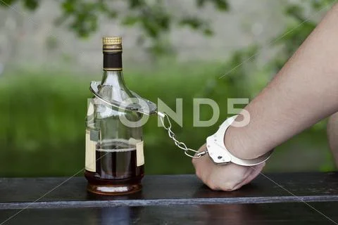 Man in handcuffs interconnected with a bottle of alcohol Stock Photos