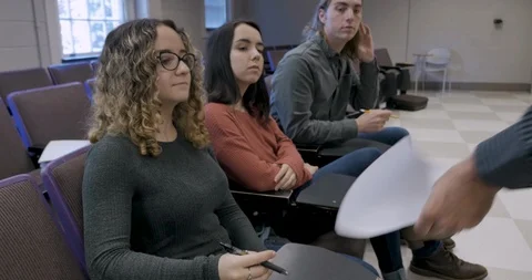 Man handing out papers to three young students sitting in a classroom Stock Footage 105908788